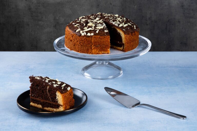 Chocolate cake with chocolate topping and white chocolate shavings on a glass cake stand.